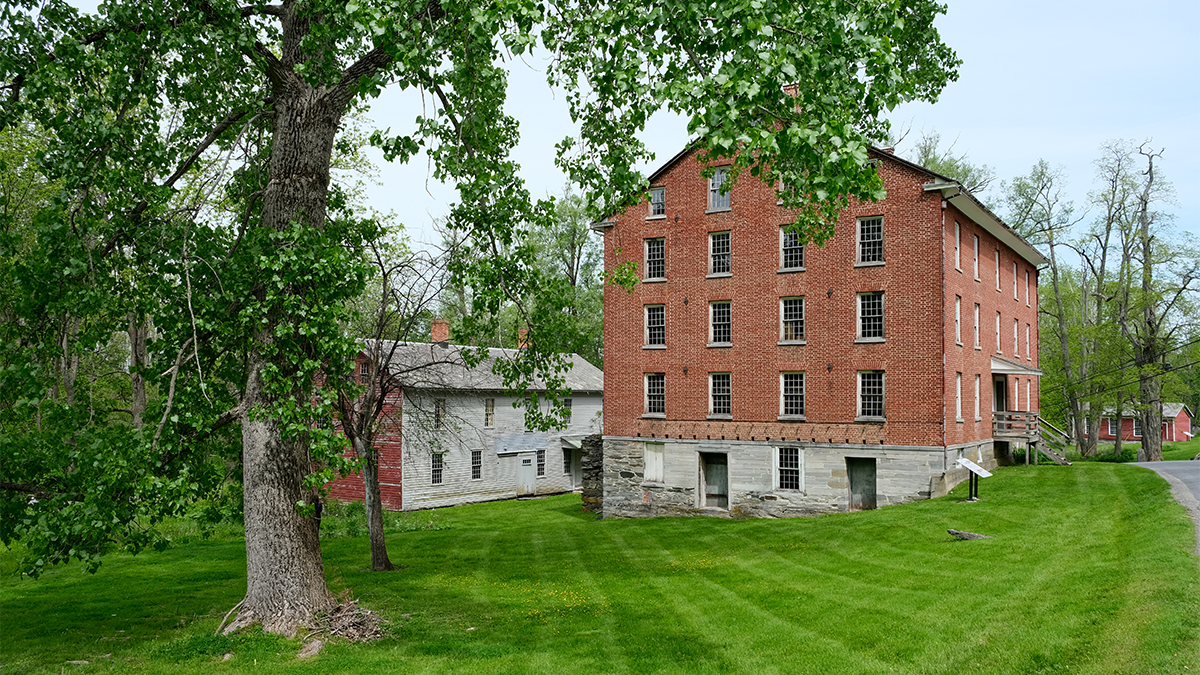 Two brick buildings site on sloped lawn; trees in foreground