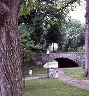 {Image: View of children playing on path leading under an old stone bridge}