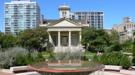 Clarke-Ford House with fountain in front of it; plants and distant buildings surround.