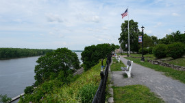 River on the left; pathway with bench in front of a sloping hill on the right