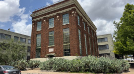 Exterior of brick building surrounded by trees, shrubs, and cacti; car in bottom left