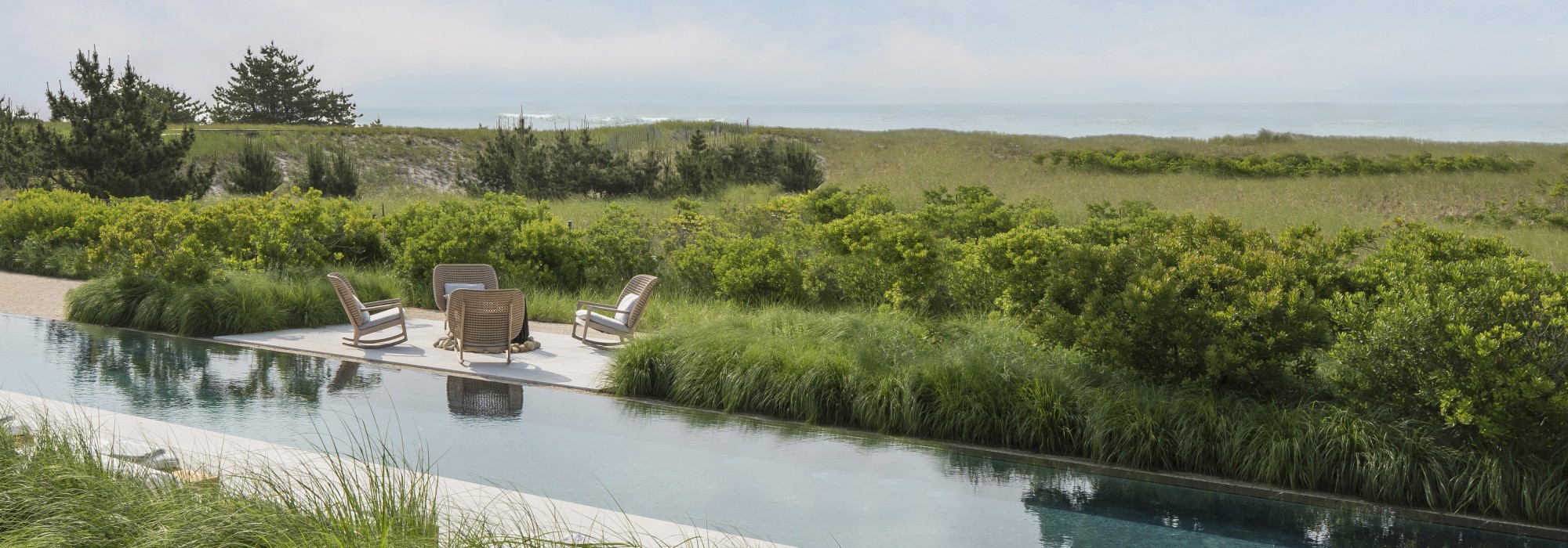 A pool in a field with a patio and chairs. 