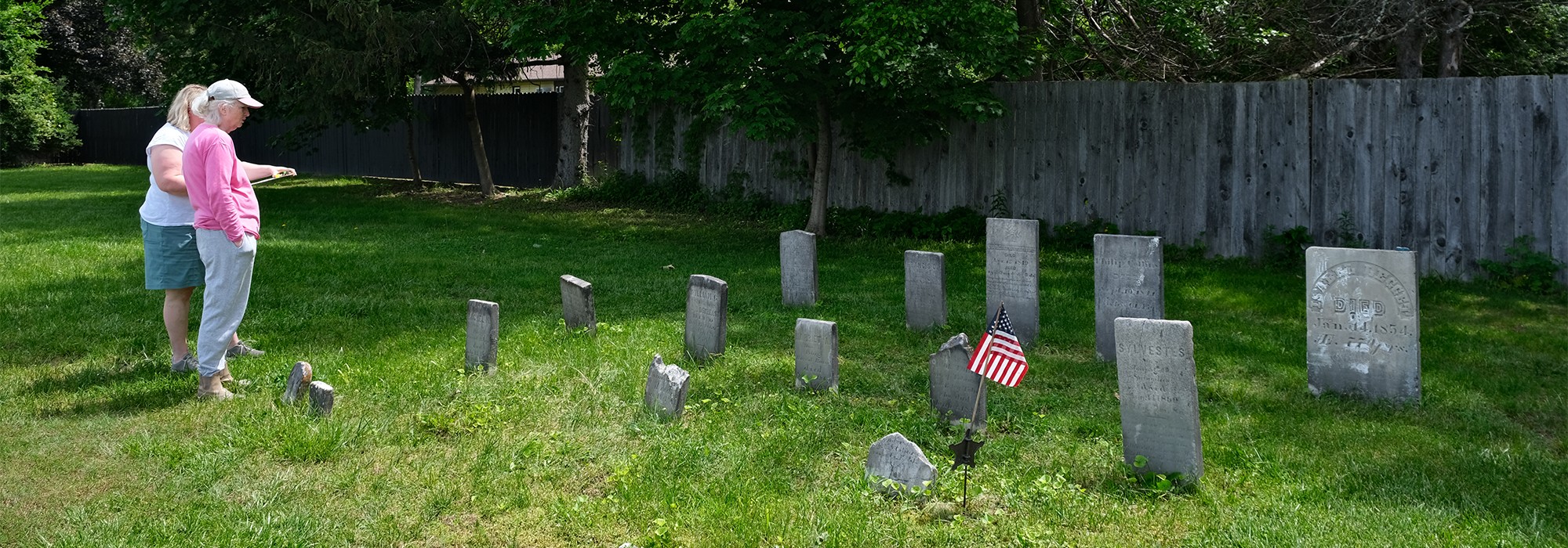 Two women stand on the left looking at cluster of gravemarkers