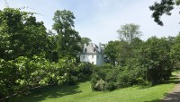 Grassy hill in the foreground, mansion in the background surrounded by trees.