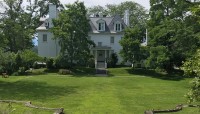 Mansion surround by trees, large lawn with low, stone walls.