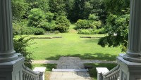View from the front steps of the mansion, large lawn with low, stone walls in the background.