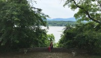 Flagstone terrace with trees on either side and borrowed views of the Hudson River and Catskill Mountains in the distance.