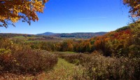 Broad views of a valley of meadows and autumnal trees; mountains in the distance