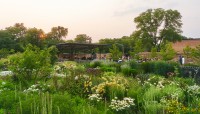 Flowering plants and shrubs in foreground; pavilion and trees in background.