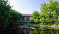 Pond in the foreground, building surrounded by trees on its shore