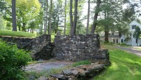 Stone wall and staircase enclosing small patio; house and trees in background