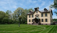 Historic house set in a lawn with a circular path in front; trees in background