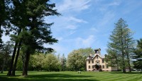 Cluster of trees on the left in foreground; house on the right in the distance; trees surround