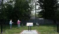 Signage in center; grave markers behind it; two women stand on the grass beside them