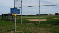 Signage in the grass outside of a baseball diamond.
