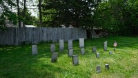 Grave markers situated in the lawn with a fence behind them; trees in the background