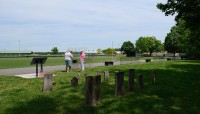 Grave markers in the foreground; women standing in the back; street and sports fields beyond