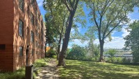 Brick building on the left, sloping lawn with trees on the right, river in the distance