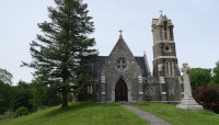 Stone chapel on top of a slope with a grave marker and tree on either side