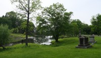 Grave markers and trees sit in lawn surrounding a pond