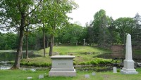Grave markers and a tree sit on a bank above a pond