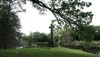 Tree branch arcs over a grave marker on the bank of a pond