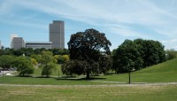 Sloping lawn with paths and trees; buildings in background