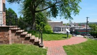 Brick pathways lead to staircase on the left; city visible in the distance