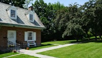 Smaller red brick building on the left; lawn and pathways on the right with trees