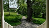 View down the front porch steps to pathways and a bench under a tree