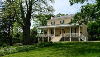 Yellow house sits on a broad lawn surrounded by trees; pathway on the left