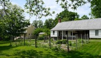 Two wood buildings on the right; fenced in garden in center; trees in background