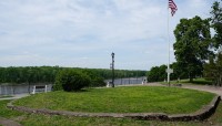 Oval lawn with stone border; flag and trees surround; river visible in the distance on the left