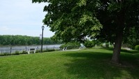 Shade tree on the right on the lawn; benches and pathway on the left; mountains and river in distance