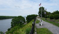 River on the left; pathway with bench in front of a sloping hill on the right