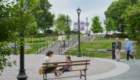 People interact in the circular plaza; staircase in background; trees surround