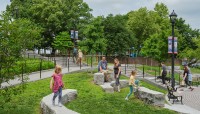 Adults and children interact with the amphitheater seating in the circular plaza; trees in background