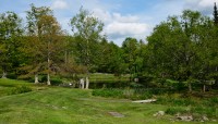 Sloping lawn leads to pond; trees surround