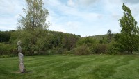 Stone sculpture on the left in a broad lawn; trees on the hill in the background