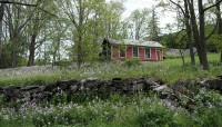 Stone wall and wildflowers in foreground; red, wood building and trees in background