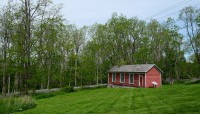 Wood building on sloping lawn; trees in background