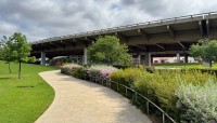 Winding pathway edged by sloping lawn leading under an overpass