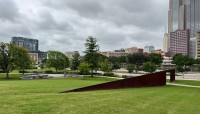 Sloping lawn with metal passageway; seating area; trees and buildings in background
