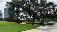 Statue of John Carpenter next to sloping lawn with trees; metal passageway in background