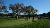 People gathered around the green; trees in background