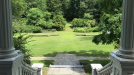 View from the front steps of the mansion, large lawn with low, stone walls in the background.
