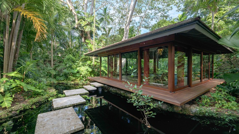 Small glass and wood building over a small pond.